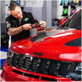 Person working on a red Jeep car with a tool in a garage setting