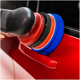 Car polisher with blue buffing pad on a red car surface.