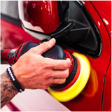 Person using a car polisher with yellow foam buff pad on a red car