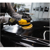 Person using a yellow and black power sander on a black surface with a blurred workshop background.