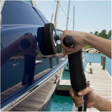 Person applying wax on a boat hull with water and boats in the background